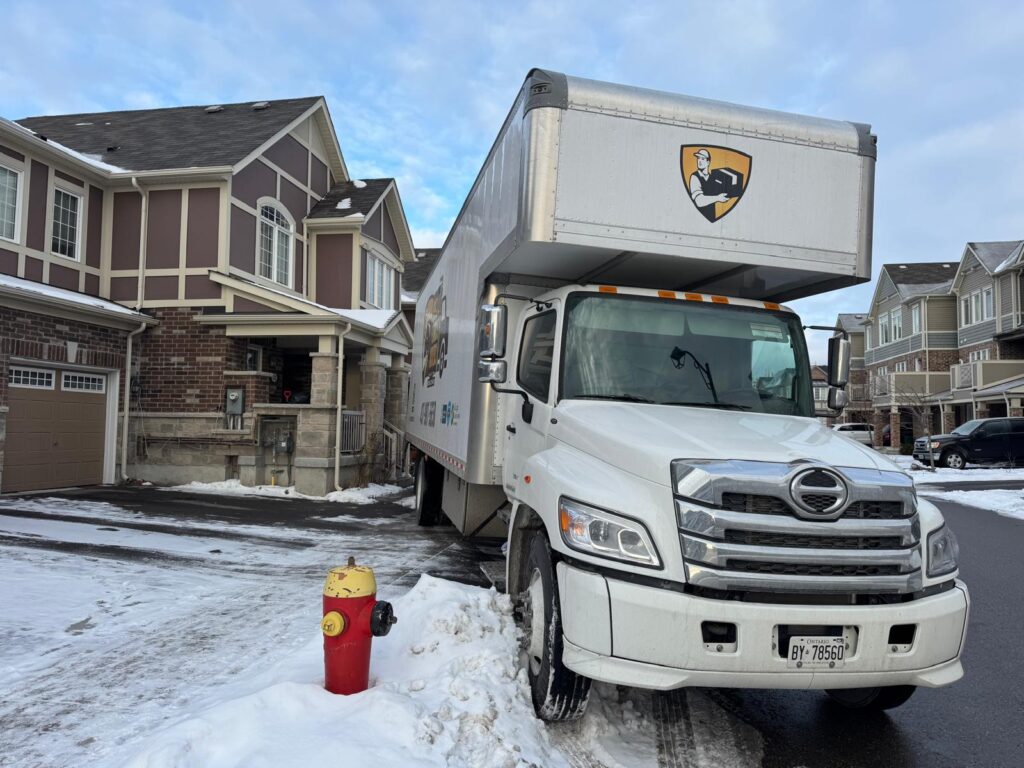 White moving truck parked near residential buildings on a snowy winter day.