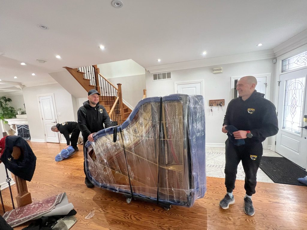 Professional movers handling grand piano transportation and moving service in a residential home.